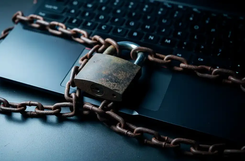 Zwaar ijzeren hangslot en verroeste ketting om een laptop, symbool voor cyberbeveiliging, op donker bureau met koud blauw zijlicht.